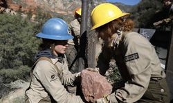 Two crew members hand off a large rock in desert canyon